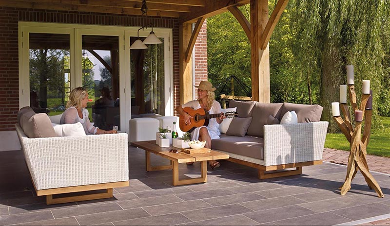 an image of an outdoor patio with two people sitting on couches, one person is playing guitar